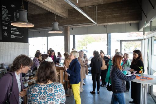 Gruppe von Frauen in einem modernen Café mit Bartheke, Hängelampen und großen Fenstern im Hintergrund.