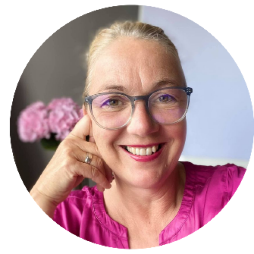 Lächelnde Frau mit Brille und blonden Haaren in pinkfarbenem Oberteil, Hand ans Gesicht gehalten.