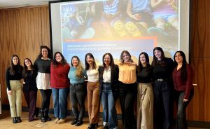 Gruppe von elf Frauen steht lächelnd vor einer Präsentationsleinwand mit deutschem Text in einem Konferenzraum.