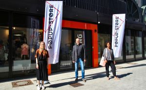 Drei Personen stehen vor einem Popup-Store mit weißen Fahnen und orangefarbenem Eingang.