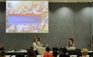 Drei Frauen auf einem Podium vor einer Leinwand mit deutschem Text und Hannover-Logo, Publikum im Vordergrund.