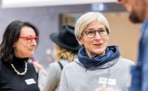 Drei Personen unterhalten sich auf einer Veranstaltung. Eine Frau mit kurzen blonden Haaren und Brille trägt ein Namensschild.