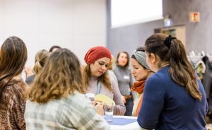 Mehrere Frauen sitzen an einem Tisch und betrachten gemeinsam ein gelbes Objekt in einem Innenraum.