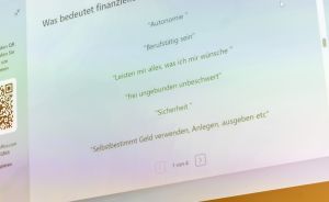 Präsentationsfolie auf Bildschirm: „Was bedeutet finanzielle Unabhängigkeit?" mit deutschen Stichpunkten zu Autonomie und Sicherheit.