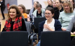 Mehrere Frauen sitzen in Stuhlreihen bei einer Veranstaltung. Zwei im Vordergrund lächeln.