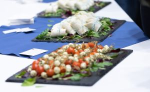 Catering-Buffet mit Platten auf weißer Tischdecke: Caprese-Salat mit Tomaten und Mozzarella, Rollen mit Salat.