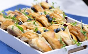 Tablett mit belegten Brötchen, garniert mit Blaubeeren und Kresse, auf blauer Tischdecke bei einem Buffet.