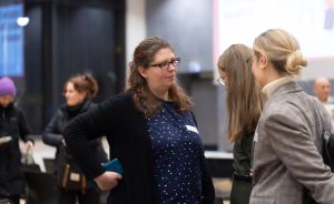 Drei Frauen stehen zusammen und unterhalten sich in einem Veranstaltungsraum. Im Hintergrund weitere Personen.