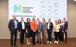 Gruppe von 10 Personen posiert vor einer Präsentationswand mit dem Logo „Fachkräfte Allianz Hannover" und Unterschriften.